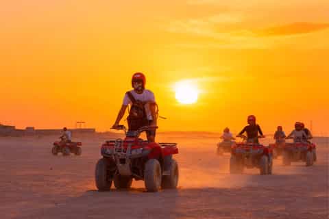 Quad bikers crossing desert terrain at sunset