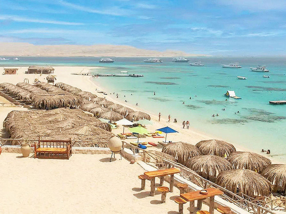 Sandy island beach with shaded seating and clear Red Sea water